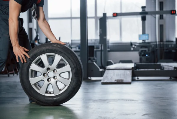 Mechanic rolling a tire past a wheel alignment rack in an auto shop