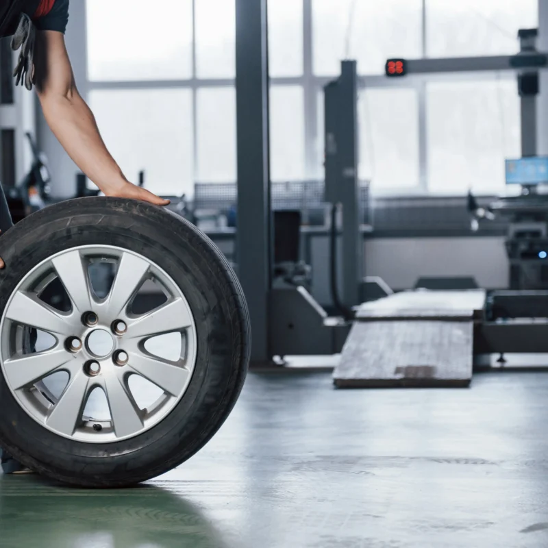 Mechanic rolling a tire past a wheel alignment rack in an auto shop