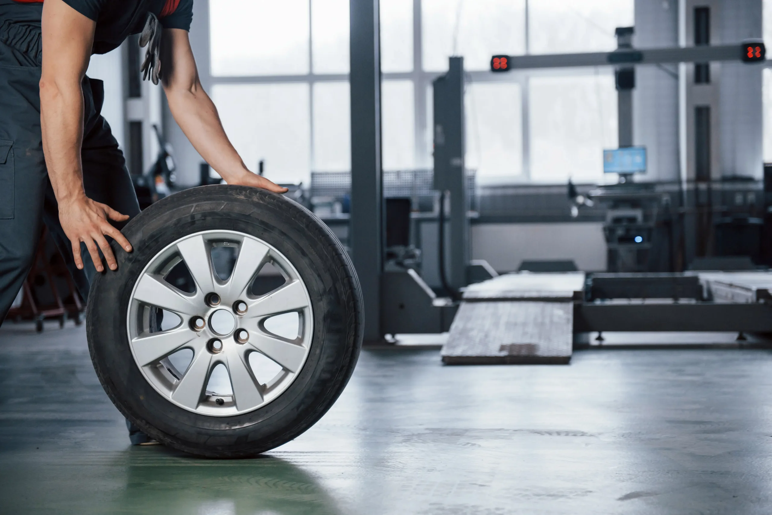 Mechanic rolling a tire past a wheel alignment rack in an auto shop