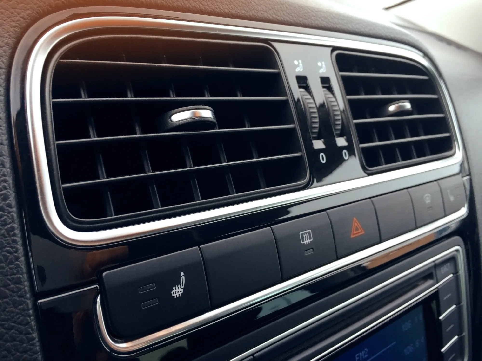 Close-up of a car dashboard showing chrome-trimmed air vents, climate controls, and heated seat and hazard light buttons.